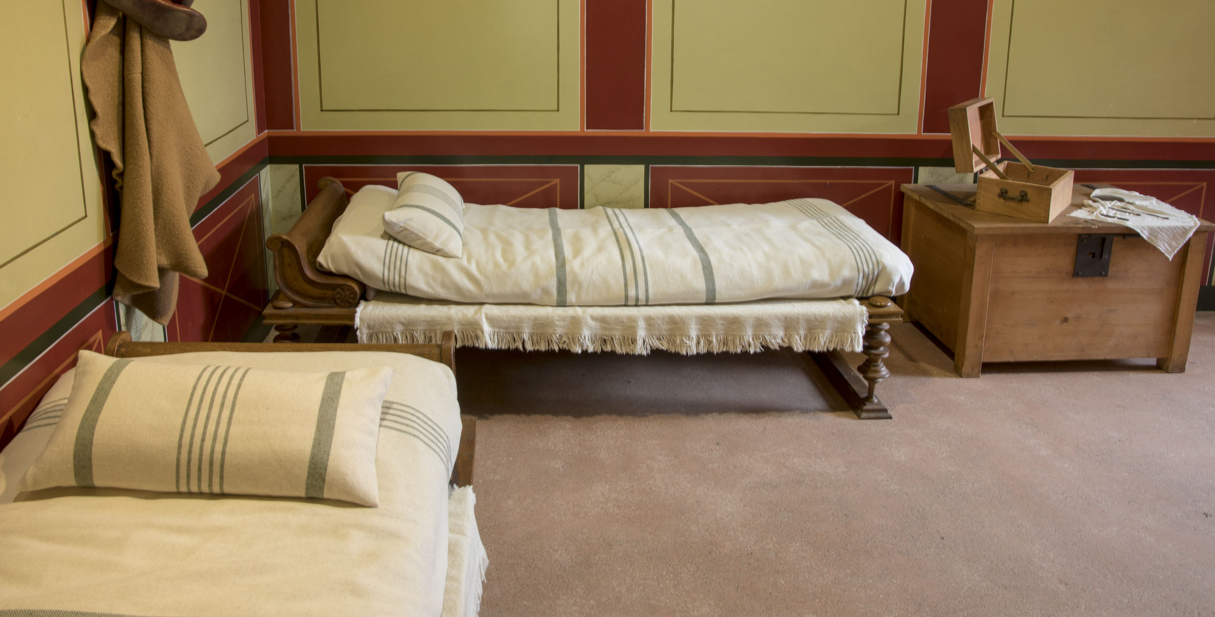 Das Foto zeigt einen Raum in Augusta Raurica mit Replikationen von römischen Betten. Die Bettbezüge sind weiss mit hellgrauen Streifen.